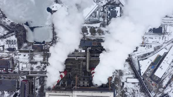 Aerial View of Two Big Red and White Factory Pipes Rising Over the Snowy Industrial Cityscape alt
