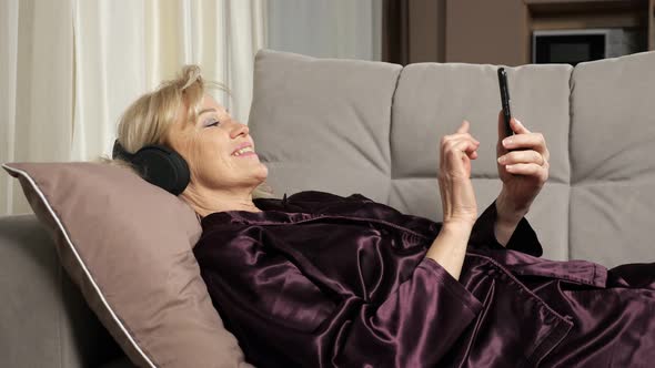 Elderly Woman Reads News Listening to Music Via Headphones