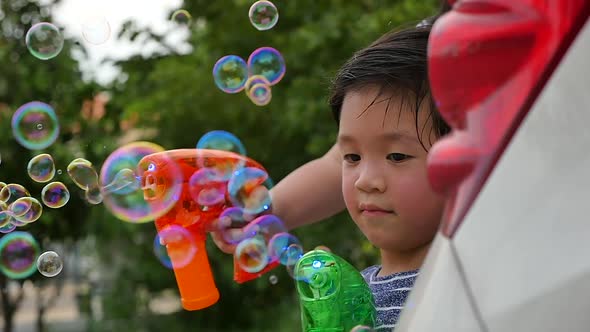 Cute Asian Child Shooting Bubbles From Bubble Gun Behind A Car Slow Motion