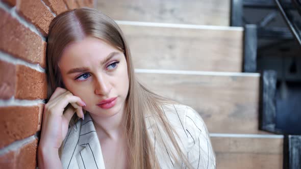 Closeup Face of Disappointed Young Beautiful Woman Sitting on Stairs at Loft Wall Background