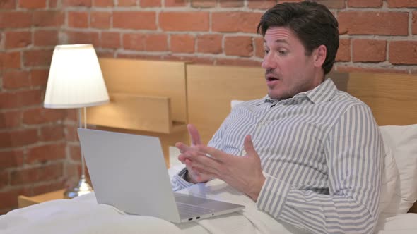 Middle Aged Man doing Video Call on Laptop in Bed