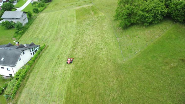 Farmer mowing green young meadows for fresh food for cows. Aerial 4k view.