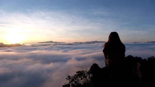 Slow motion of a female traveler sitting on the mountain peak, watching sunrise and sea of fog