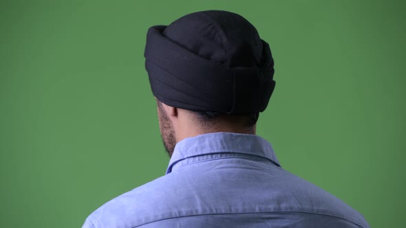 Profile View of Young Handsome Bearded Indian Businessman Wearing Turban and Looking Back