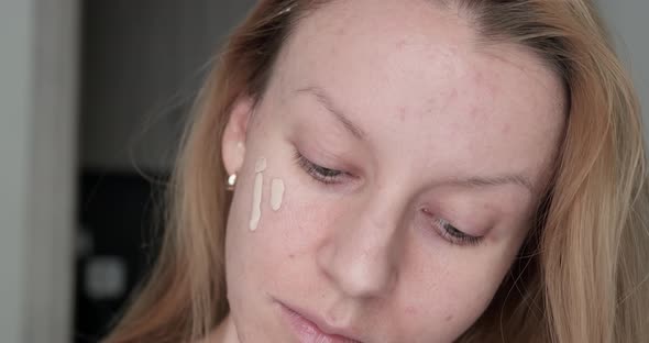 Woman applying make up foundation on face.
