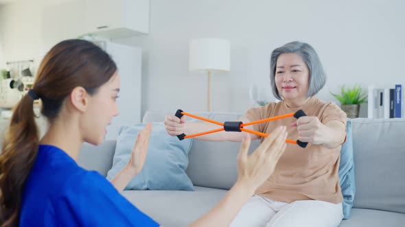 Asian Disabled old woman doing physiotherapist with support from nurse in living room at home.