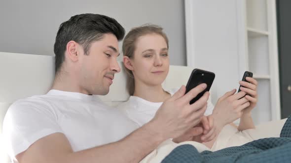 Happy Couple Using Smartphone in Bed