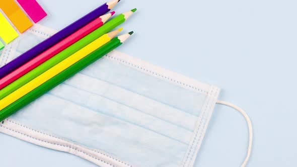 School Supplies Lie on a Pastel Blue Background with a Medical Mask