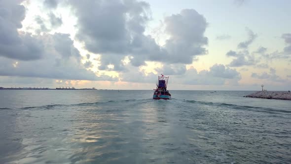 A slow aerial shot from a drone following a fishing boat exiting a local bay and cruisng towards the