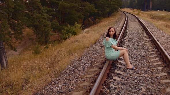 Thoughtful Woman Sits on Railway in Countryside
