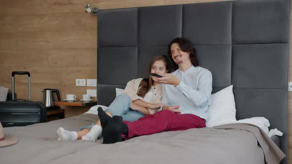 Girl and Guy Watching TV in Bed in Hotel Room Relaxing During Vacation Together