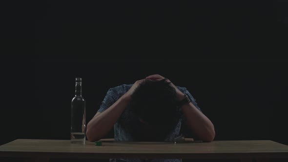 Drunk, Depressed Asian Man Pouring Vodka In A Shot Glass Before Drinking In Black Background