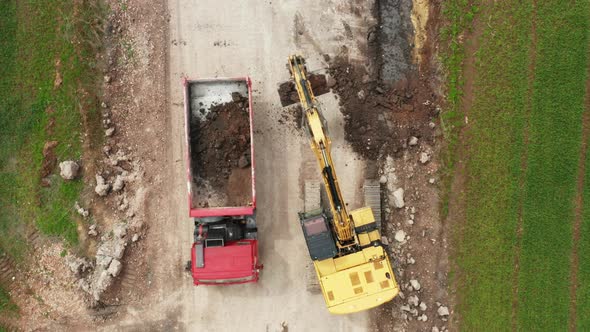 Top View Yellow Excavator Picks Up Land From the Field and Loads It Onto a Red Truck