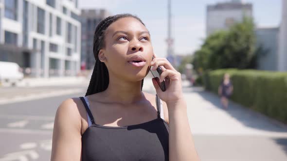 A Young Black Woman Talks on a Smartphone - a Townscape in the Blurry Background