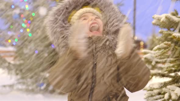 Portrait of happy girl in winter in fur hood against background of fairy lights, Christmas trees