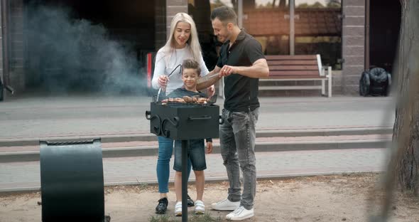 Happy Family Cook Meat on Grill. Father and Mother with Son Fry Sausages on Grill and Smiling