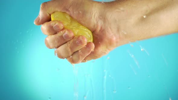 Hand Squeeze Fresh Lemon in Slow Motion on Blue Background