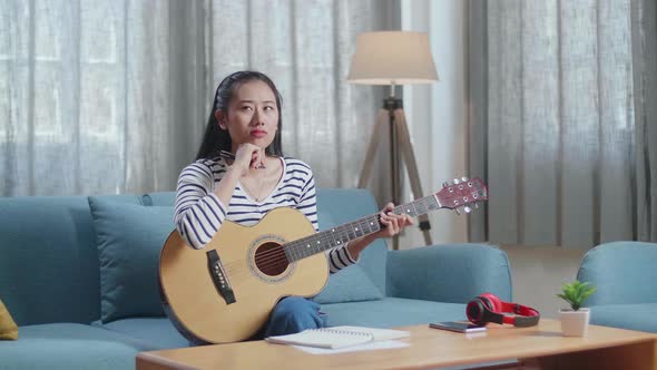 Asian Woman Composer With A Guitar Thinking Before Composing Music On Paper At Home