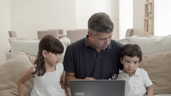 Cheerful Dad and Two Cute Kids Sitting on Couch at Laptop