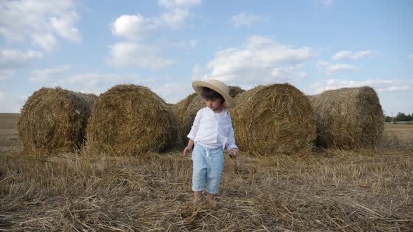 Boy in a White Shirt and a Straw Hat Is Barefoot on a Sloping Field