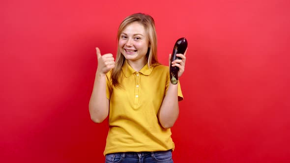 Cute and Slightly Fat Girl in a Yellow T-shirt Holding Fresh Eggplants in Her Hand,