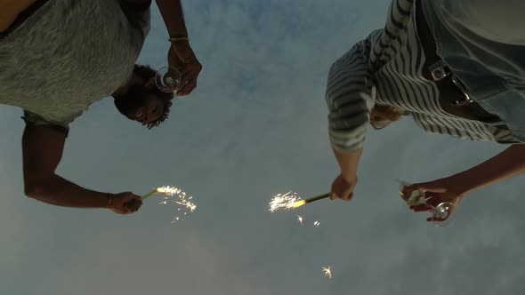 Under view of couple waving with firework candles and holding champagne glasses