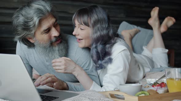 Husband and Wife Happy People Using Laptop Lying in Bed and Talking Enjoying Leisure Time Together