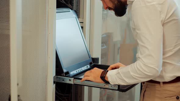 IT Engineer Working On Computers Console In A Server Room. Man Using Console Computer In Server Room