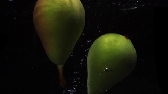 Two Pears Falls Into the Water with Splashes and Bubbles in Slow Motion.