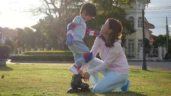 Asian Mother Helping Her Son Putting His Roller Skates On Enjoying Time Together In The Park