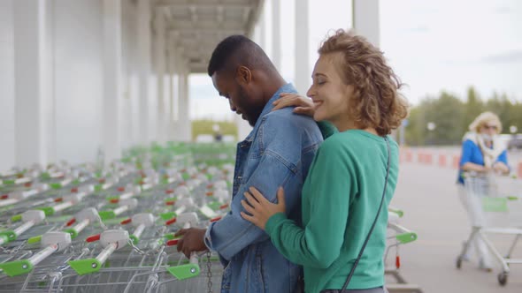 Side View of Young Multiethnic Couple Taking Shopping Cart Near Store Entrance