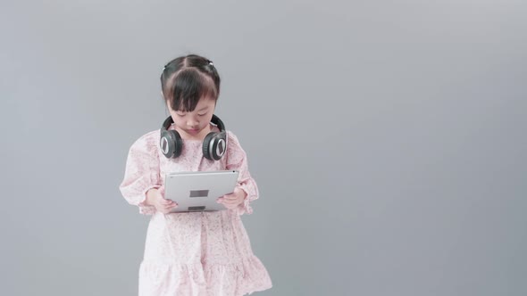 Child with headset watching videos with digital tablet. Gray Background with Copy Space.