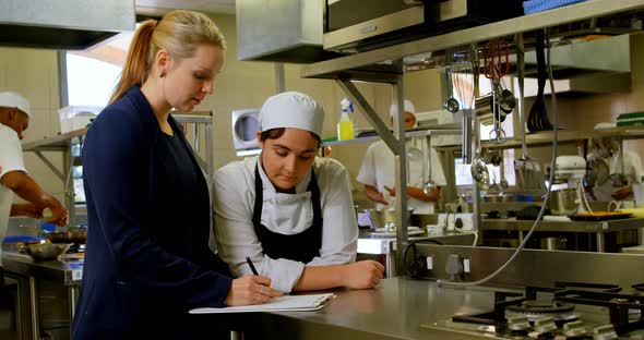 Female manager and female chefs discussing over clipboard 4k