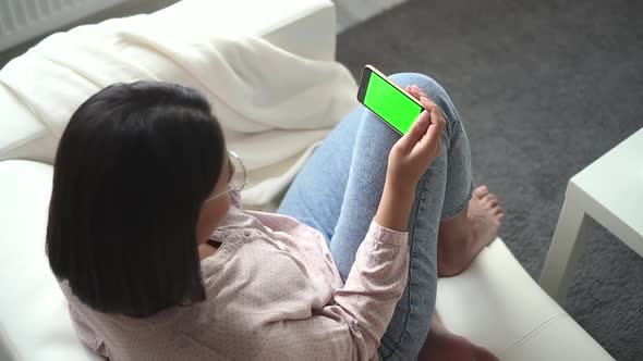 Woman Sits on Sofa and Holds Smartphone Screen in Front of at Home Spbd