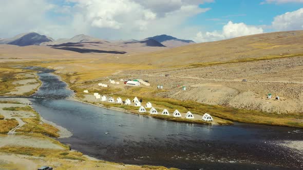 Aerial drone panning across a natural river with white luxury glamping tents in the high-altitude al