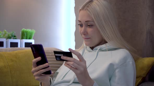 Young female customer using mobile phone while sitting on sofa at home.