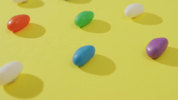 Video of close up of rows of multi coloured sweets over yellow background