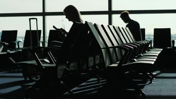 People at the Airport Terminal Are Waiting for Their Flight. Silhouettes on the Background of the