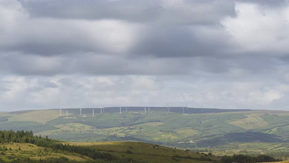 Time lapse of distant hills with forest and wind turbines on a cloudy summer day in Ireland. alt