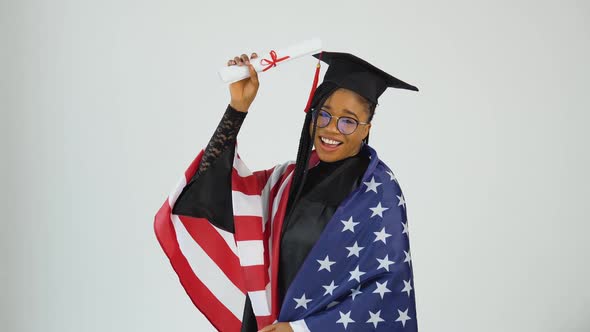Happy Stylish Afro American Woman Student In Graduate Uniform Shows Diploma Holding USA Flag On