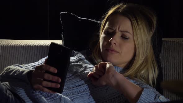 A Young Beautiful Woman Lies on a Couch in a Dark Room and Works on a Smartphone - Closeup