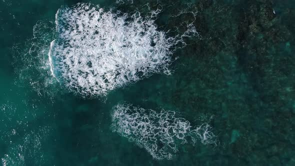 Drone descending above ocean waves crashing above the reef in hawaii