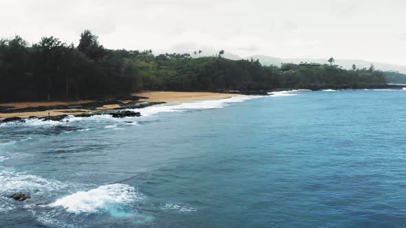 Aerial camera slowly approaches sandy shore with a dense forest on a rainy day at Kauai, Hawaii, USA