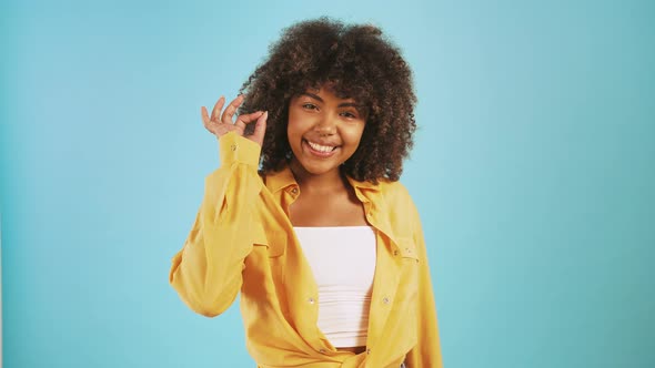 Young Afro American Woman is Smiling and Showing Okay Hand Gesture While Posing Against Blue