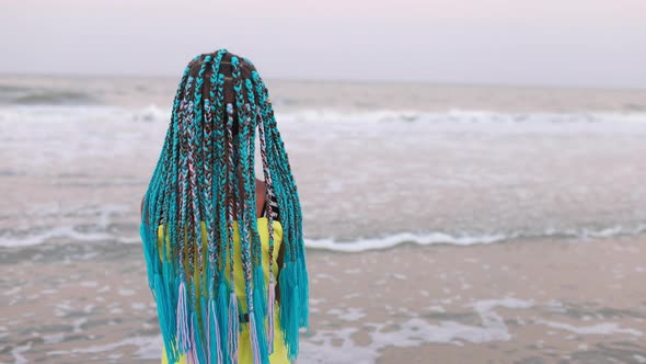 A Girl in a Summer Suit with African Braids Looks at the Sea Horizon While Standing on the Beach