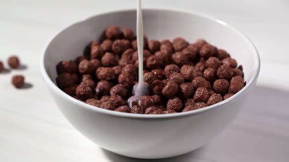 Chocolate balls corn flakes with milk in white bowl, white background