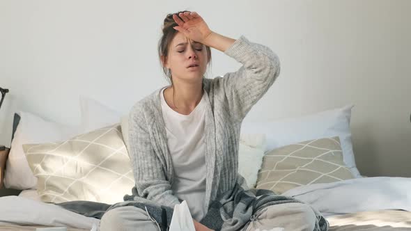 Sick Young Woman Sitting in Bed with Flu and Huge Headache