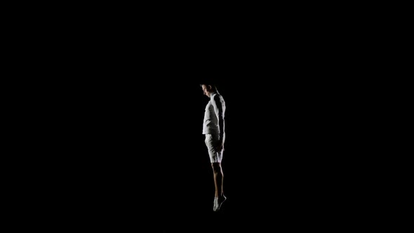 Handsome Male Gymnast in White Clothes on a Black Background Jumping on a Trampoline in Slow Motion