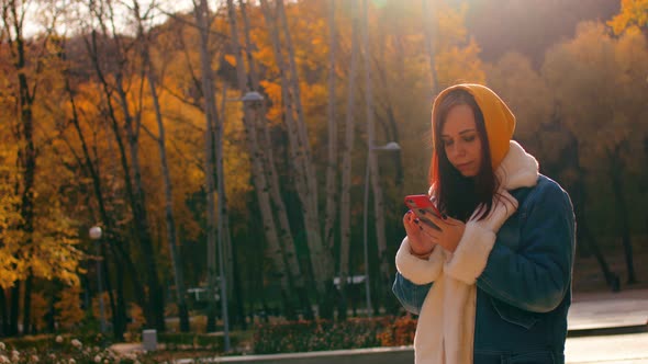 Young Woman Standing with Mobile Phone in City Park