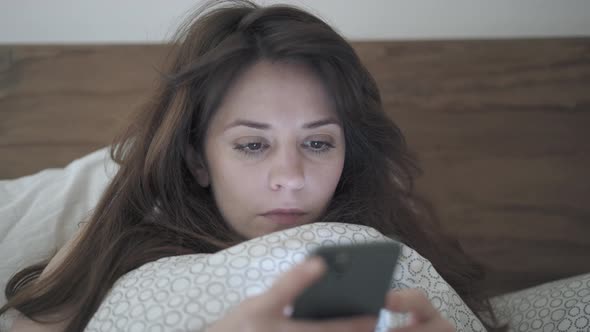 Handheld Shot of Woman Scrolling a Phone Lying in a Bed